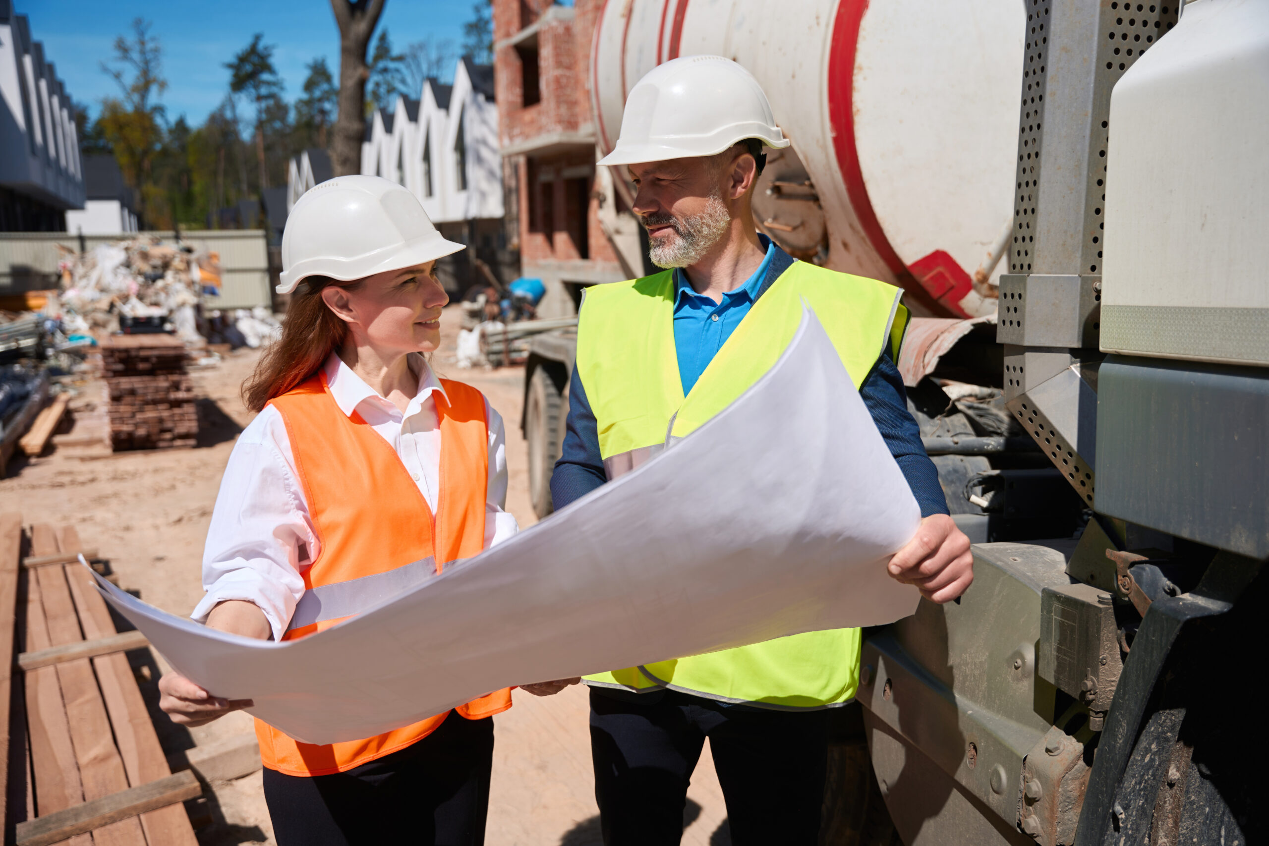 High qualified architect showing blueprint of construction site to foreman, workers in safety vests and hardhats discussing project